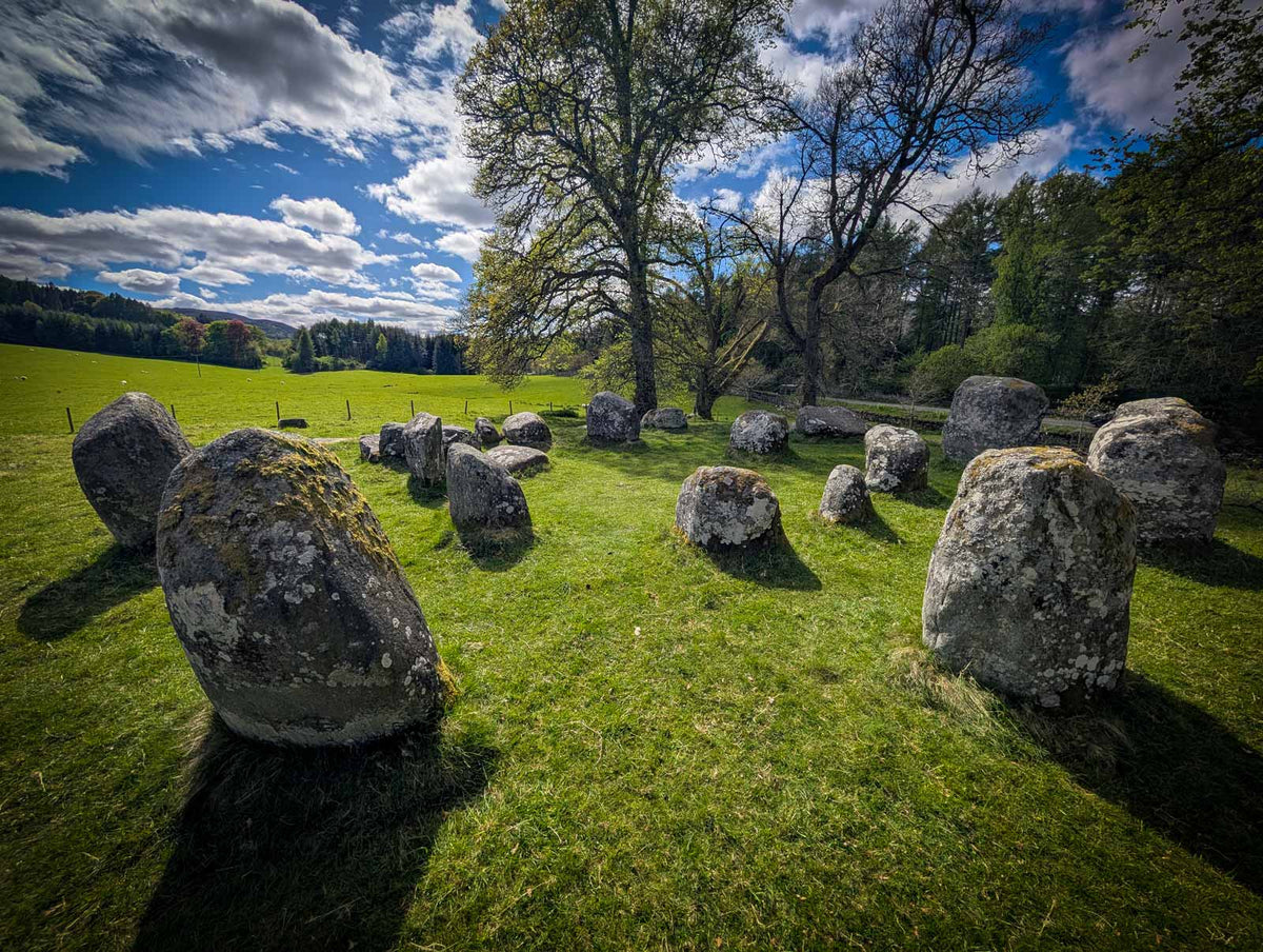 A stone circle with several tall standing stones in a grassy park, with trees and a dark sky in the background.