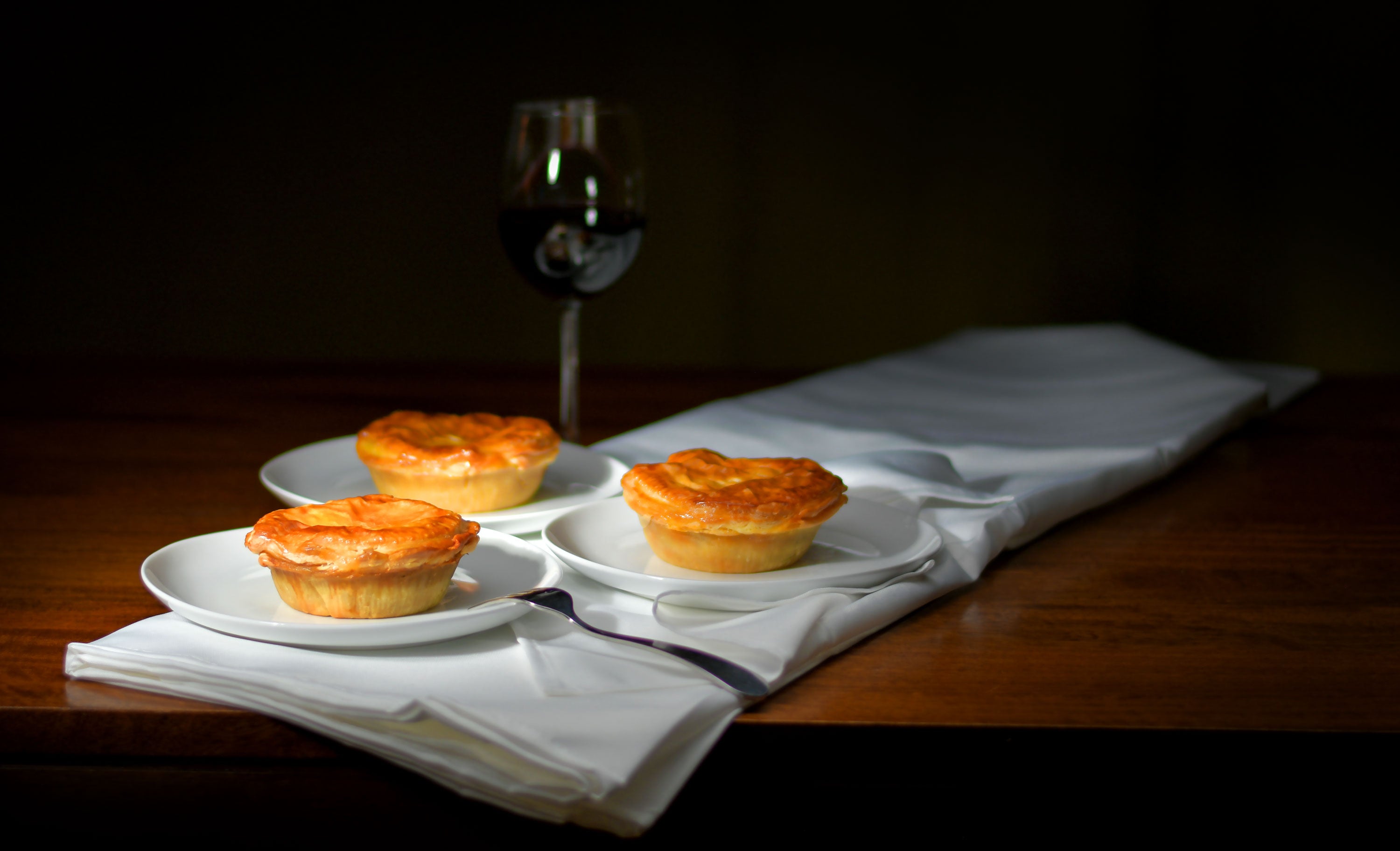 Three savory pies on a table with glass of wine